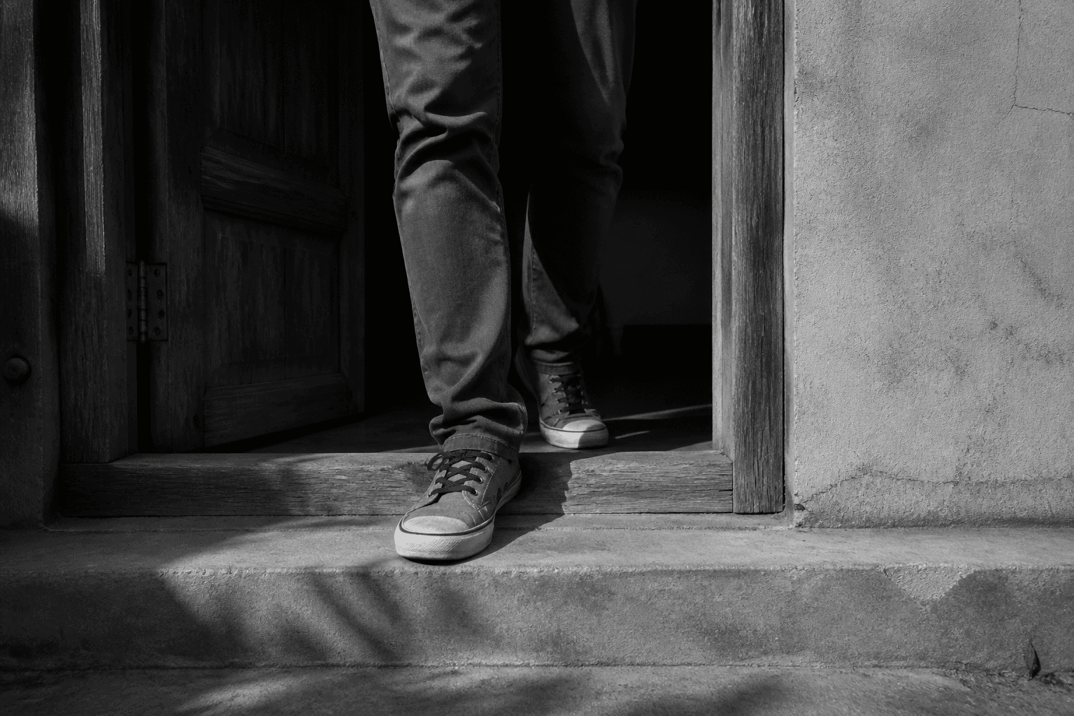 A person steps across a doorway, with muted red laces on the leading shoe in an otherwise black-and-white image.