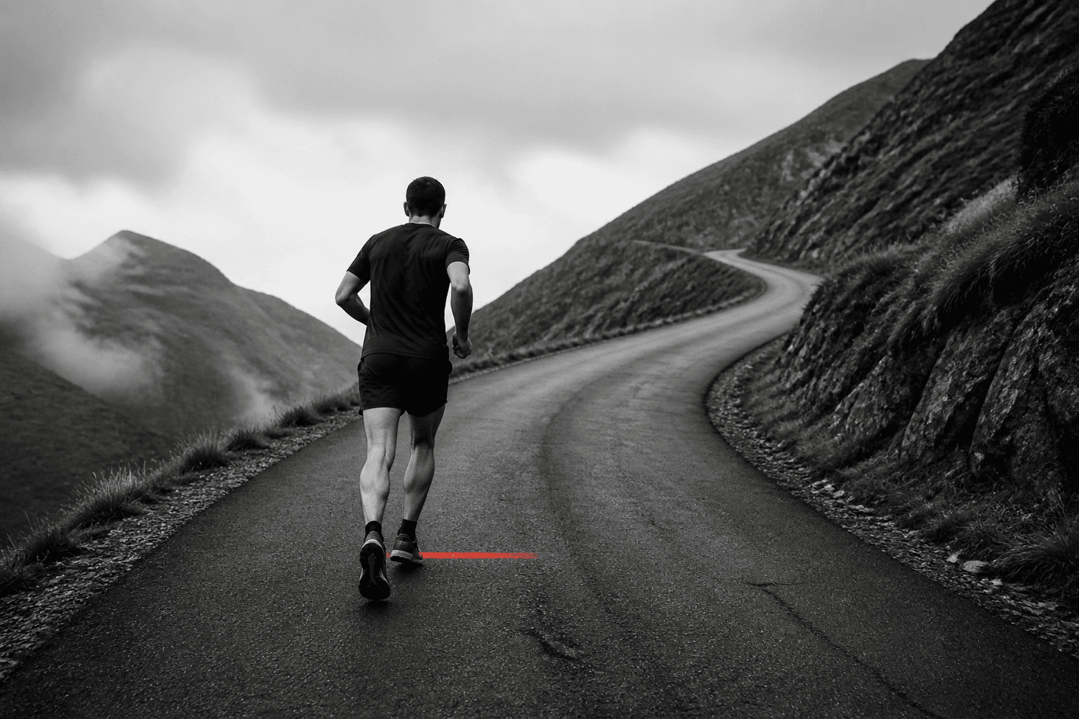 A runner climbs a steep mountain road and steps across a short red stripe on the asphalt.